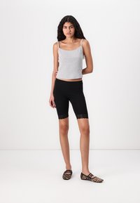 Grå bomulds tank top og sorte shorts til knæet med blondekant. Modellen bærer leopardmønstrede flade sko. Simpelt, tætsiddende design.