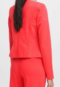 Röd kavaj med skräddarsydd passform, texturerat tyg och långa ärmar. Har en skåra bak och slät finish, tillsammans med matchande byxor.