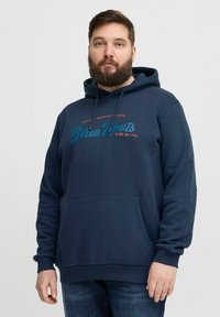 Sötétkék kapucnis pulóver pamut keverékből, elülső zsebbel; a mellrészen "Blue Roots" grafika látható türkiz és narancs színben.