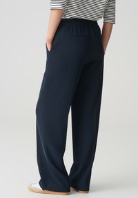 Marineblauwe wijde broek van soepel stof heeft een elastische tailleband en zijzakken, met een relaxte pasvorm en strakke lijnen.