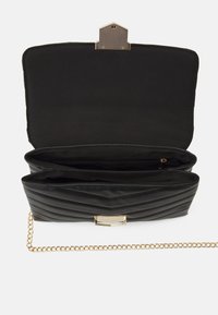 Černá prošívaná kabelka se zlatým řetízkovým popruhem. Má zapínání na cvok a prostorný vnitřek se dvěma přihrádkami. Hladká textura.