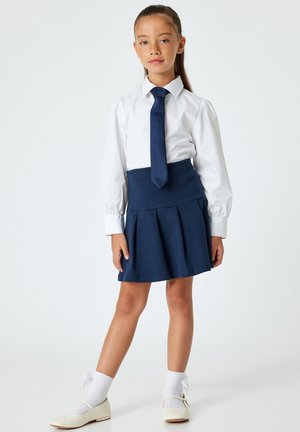 Witte blouse, marineblauwe geplooide rok, marineblauwe stropdas, witte sokken en beige ballerina's. Gladde stof met een getailleerde pasvorm en nette afwerking.