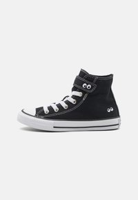 Zapatilla alta de lona negra con puntera y suela de goma blanca, que cuenta con cordones y costuras blancas, y una correa de Velcro con dos ojales decorativos.
