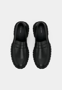 Black loafers with a rounded toe, smooth leather upper, and textured rubber sole. Features subtle stitching and a decorative band across the front.