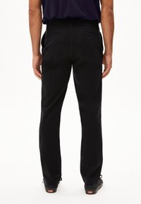 Zwarte katoenen broek met een rechte pasvorm, voorzien van twee achterzakken en een subtiele textuur. Draagt met zwarte schoenen.