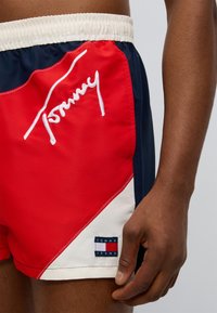 Κόκκινα και ναυτικά μαγιό με κεντημένη τη λέξη «Tommy», ελαστική ζώνη μέσης και πλακέτα με το λογότυπο «TOMMY JEANS» στο πόδι.