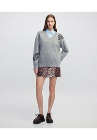Grijze gebreide trui met versieringen op de mouwen, gecombineerd met een glanzende minirok met luipaardprint en zwarte veterschoenen.