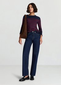 Haut à manches longues rayé bleu marine et rouge, associé à un jean large bleu foncé et des mocassins noirs. Un sac bandoulière marron complète la tenue.