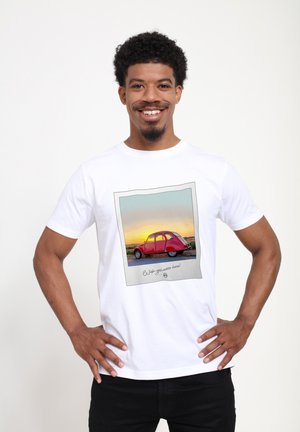 Hvid bomuld t-shirt med grafik af en rød vintage bil med en solnedgang i baggrunden, indrammet af en polaroid-lignende kant.