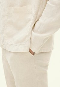 Camicia in lino leggera color beige con tasca e vestibilità ampia, abbinata a pantaloni beige testurizzati coordinati. Tessuto morbido con dettagli delicati.