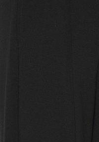 Zbliżenie na czarną tkaninę z widocznymi pionowymi liniami przeszyć, ukazujące teksturę i szczegóły szwów.