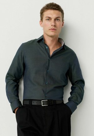 Dark green button-up shirt with a subtle texture, contrasting patterned collar, and long sleeves, paired with black trousers and a belt.