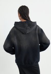 Haut à capuche noir avec un dégradé gris, présentant une grande capuche, une coupe ample, des poignets et un ourlet côtelés. Texture lisse sans logos visibles.