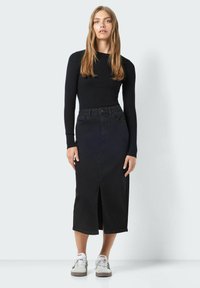 Črna rebrasta dolgosleeve majica v kombinaciji s črno denim midi krilo z razporkom spredaj. Model nosi bele superge za kontrast.