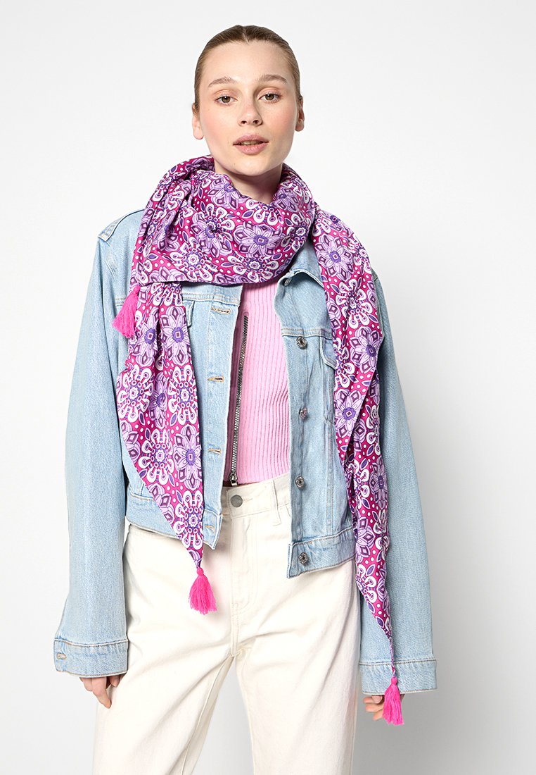 Écharpe violette et rose à motifs avec des franges, portée sur un haut pastel et une veste en denim, fabriquée dans un tissu léger et doux.