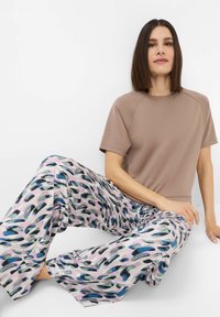 Braunes Kurzarmoberteil mit Rundhalsausschnitt kombiniert mit weit geschnittenen Hosen, die ein mehrfarbiges, abstraktes Muster in Blau- und Rosatönen aufweisen.