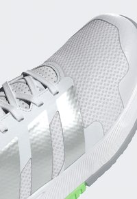 Grey and white athletic shoe with mesh upper, silver accents, and textured surface; features traditional lacing and a green sole detail.