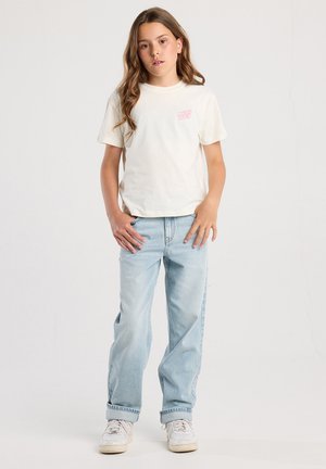 T-shirt en coton blanc avec "MALIBU BEACH" en imprimé rose, associé à un jean baggy bleu clair et des baskets blanches.