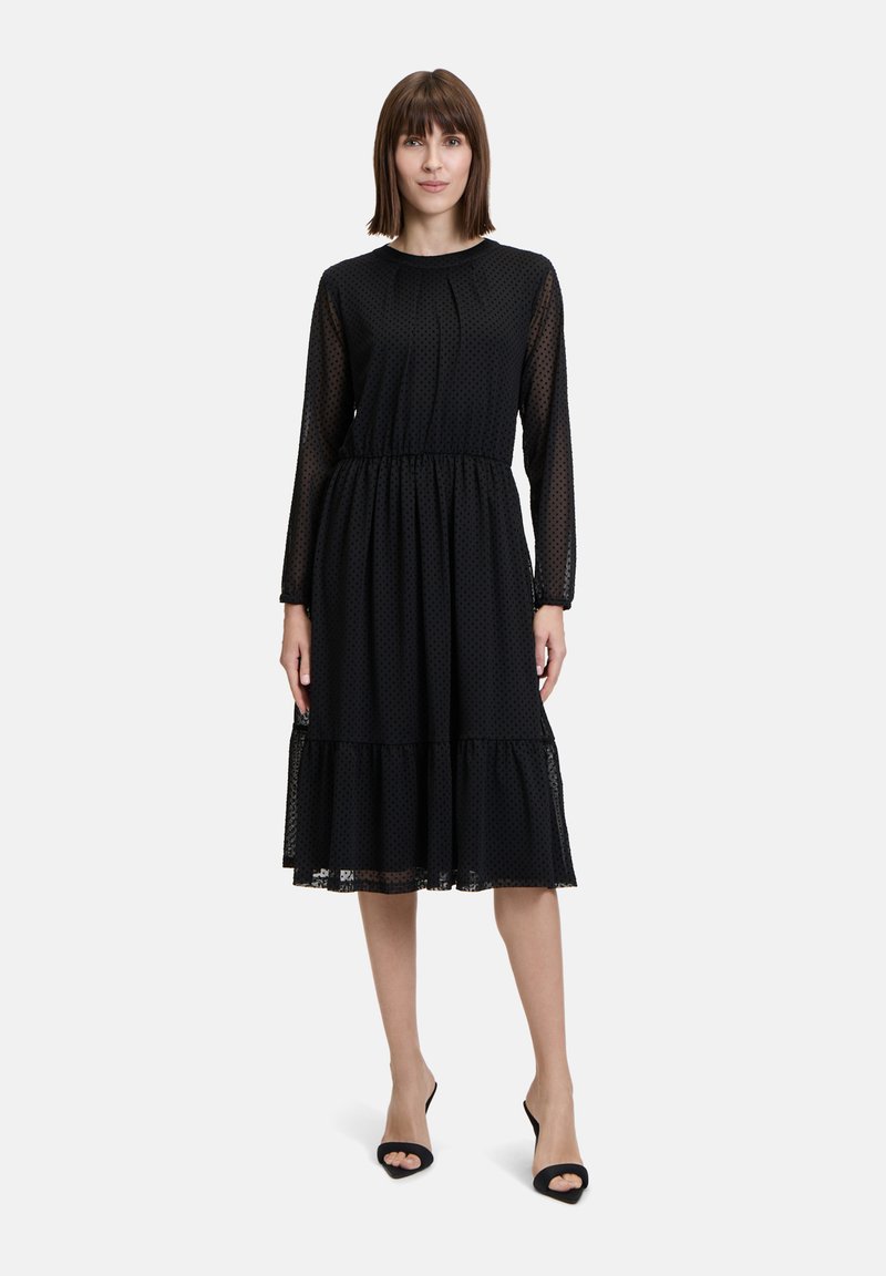 Schwarzes knielanges Kleid mit langen durchsichtigen Ärmeln, gerafftem Taillenbund und schichtsaum. Verfügt über ein dezentes Pünktchenmuster.