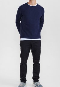 Marinblå stickad tröja med texturerat mönster, rund halsringning och långa ärmar, lager-på-lager över en vit skjorta; kombinerad med svarta byxor och gråblå sneakers.