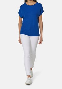 Niebieski prążkowany sweter z krótkimi rękawami, w połączeniu z białymi dżinsami i białymi trampkami. Top ma okrągły dekolt i luźny krój.