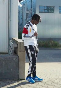 Athletic wear featuring a white long-sleeve shirt with black stripes and red and yellow accents, paired with black pants and blue shoes.