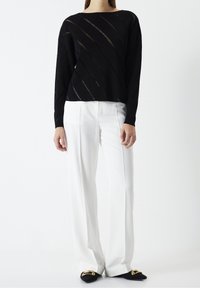 Czarny sweter dzianinowy z ukośnymi przezroczystymi paskami, w połączeniu z białymi spodniami o szerokich nogawkach i czarnymi butami z złotymi akcentami.