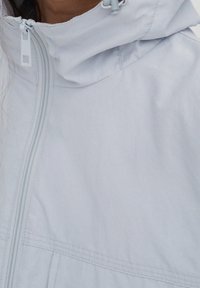 Ljusblå dragkedjejacka med hög krage, slät textur och funktionell dragkedjedetalj, lämplig för vardags- eller utomhusbruk.