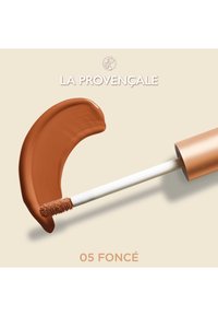 Rouge à lèvres liquide dans une teinte marron profond, avec un applicateur plat aux poils doux et un tube cylindrique doré et blanc.