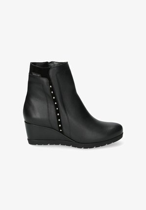 Bottine à talon compensé en cuir noir avec fermeture éclair latérale et clous décoratifs argentés le long de la ligne de la fermeture éclair.
