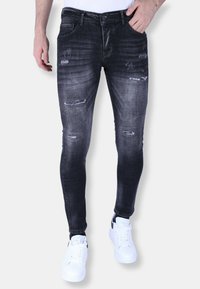 Zwarte distressed skinny jeans met vervagingdetails en scheuren aan de voorkant. Gecombineerd met witte sneakers voor een casual uitstraling.