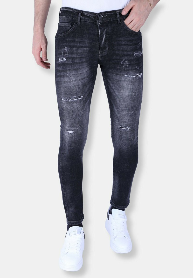 Zwarte distressed skinny jeans met vervagingdetails en scheuren aan de voorkant. Gecombineerd met witte sneakers voor een casual uitstraling.