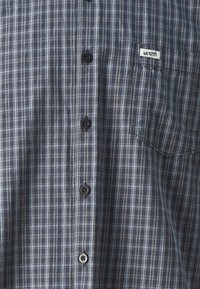 Plaid short-sleeve shirt in navy and gray tones. Features button closure and chest pocket with logo tag, fabric appears lightweight and textured.