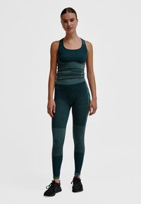 Turkos sportlinne och leggings med strukturerad design och kontrasterande paneler, kombinerat med svarta sneakers.