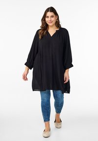 Sort tunika med V-udskæring, lange ærmer og en løs pasform, parret med blå slidte skinny jeans og beige ballerinaer.