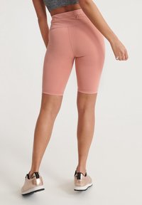 Ljust rosa högmidjade cykelshorts gjorda av elastiskt tyg med en mjuk textur. Kombination med metallic sneakers med svarta detaljer.