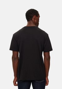 Camiseta de algodón negra con mangas cortas y cuello redondo, que presenta un corte relajado y una textura suave, vista desde la parte de atrás.