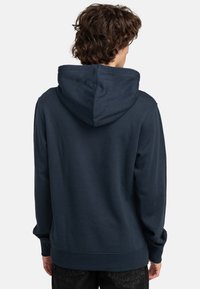 Donkerblauwe hoodie met een kangoeroezak, ribgebreide mouwen en zoom. Zachte stof met een gladde textuur, met een strak en eenvoudig ontwerp.