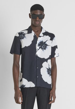 Camisa de manga corta en azul marino oscuro con grandes patrones florales en blanco y azul. Presenta un cierre frontal con botones y un diseño de cuello relajado.