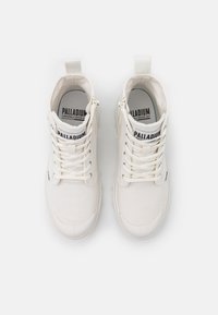 Zapatillas altas de lona blanca con cordones, cremalleras laterales y un logo en la lengüeta. Textura suave y diseño de punta redonda.