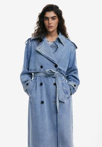 Hellblauer Denim-Trenchcoat mit doppelt umrundendem Design, großen Revers, gebundenem Gürtel und schwarzen Knöpfen.