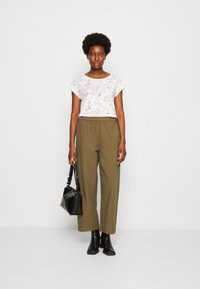 Top à manches courtes florales en blanc et couleurs pastel, associé à un pantalon large vert olive, des bottines noires et un sac à main noir texturé.