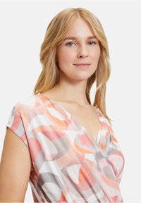 Kurzes Kleid mit V-Ausschnitt, aus leichtem Stoff mit mehrfarbigen abstrakten Kreismuster in Korallenrot, Grau und Weiß.