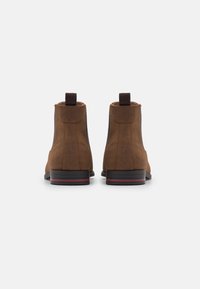 Bottines en daim marron à finition lisse, avec languette à l'arrière et accent rayé contrastant sur la semelle. Design simple avec un bout arrondi.