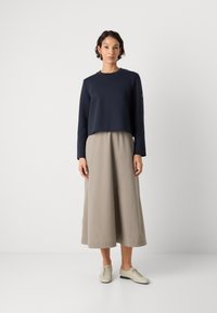 Sudadera navy corta con mangas largas y escote redondo, combinada con una falda midi fluida beige y zapatos de cordones beige claro.