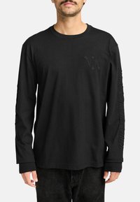 Zwarte lange mouwen T-shirt van katoen, met een subtiele 3D-logo op de borst en tekst gedrukt langs één mouw. Klassieke pasvorm.