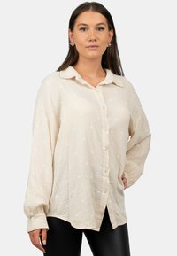 Camicia crema con bottoni, realizzata in un tessuto leggero e testurizzato, caratterizzata da pois bianchi, colletto e maniche lunghe.