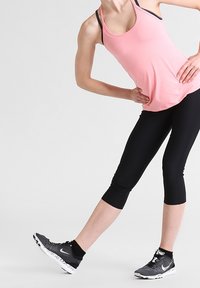 Pink athletic tank top with black straps, paired with black capris and black running shoes featuring a white sole, in an active pose.
