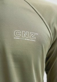 Olijfgroen prestatiehemd van gestructureerde stof met een aansluitend ontwerp. Het logo "CNZ CORE__NINE.ZERO" is prominent in het wit weergegeven.