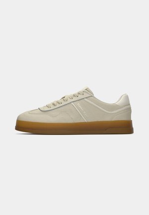 Beige low-top sneaker with gum sole, laces, and "Tommy Jeans" logo on the side, shown in side profile on white background.